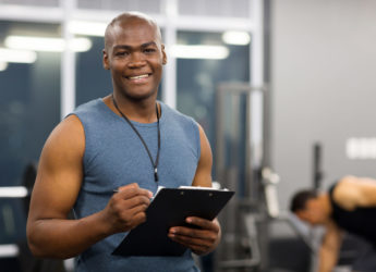 young african american male personal trainer holding clipboard in gym