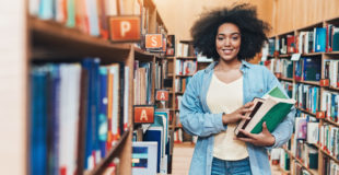 Student holding a stack of books in a library