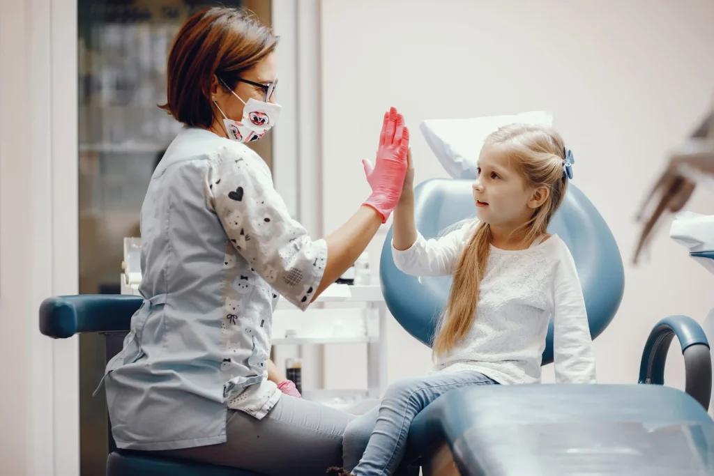 Criança feliz sentada em cadeira de dentista cumprimentando com um bater de mãos com uma Dentista